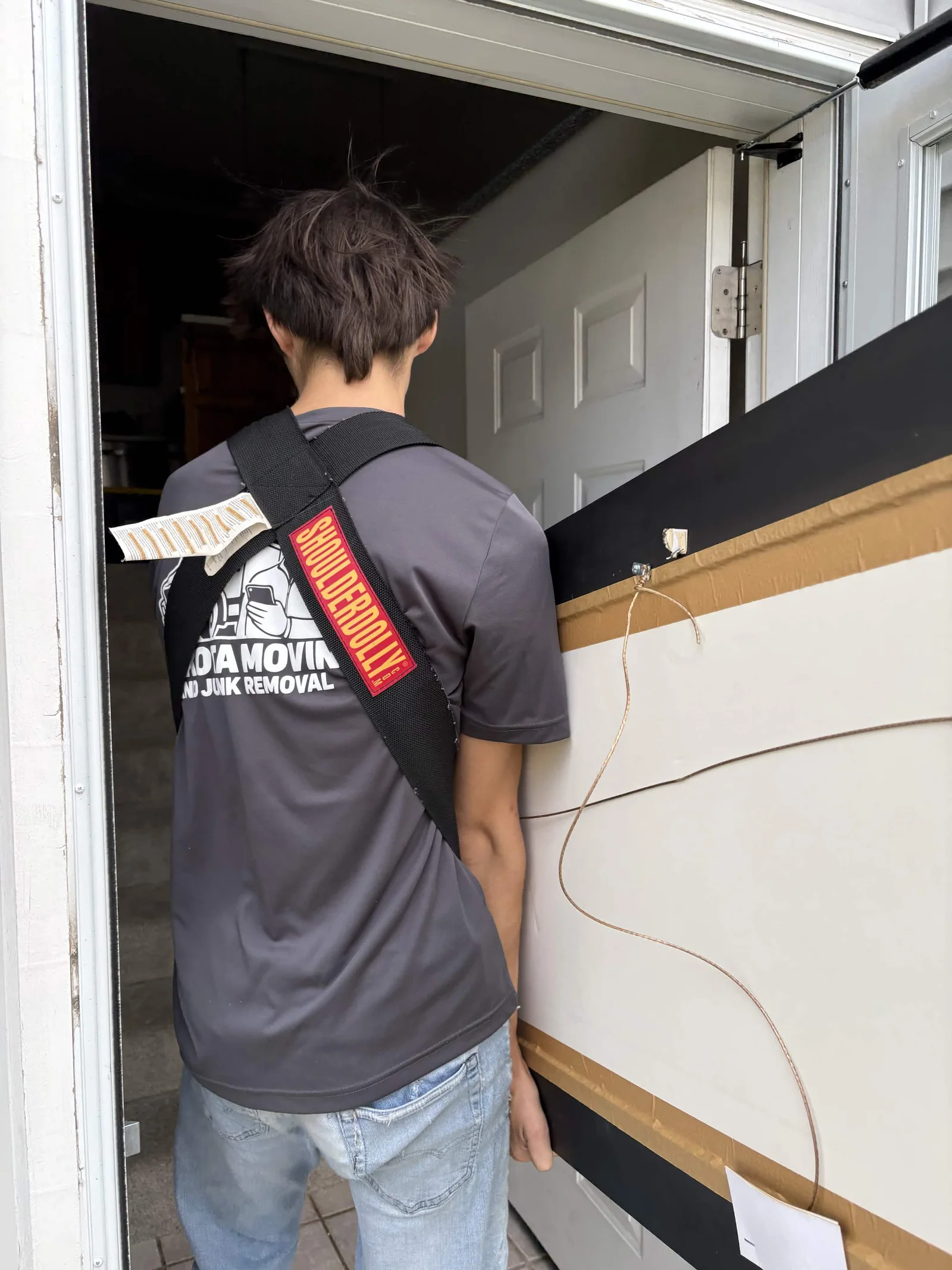 A crew member carries a large piece of furniture through a doorway with a shoulder dolly.