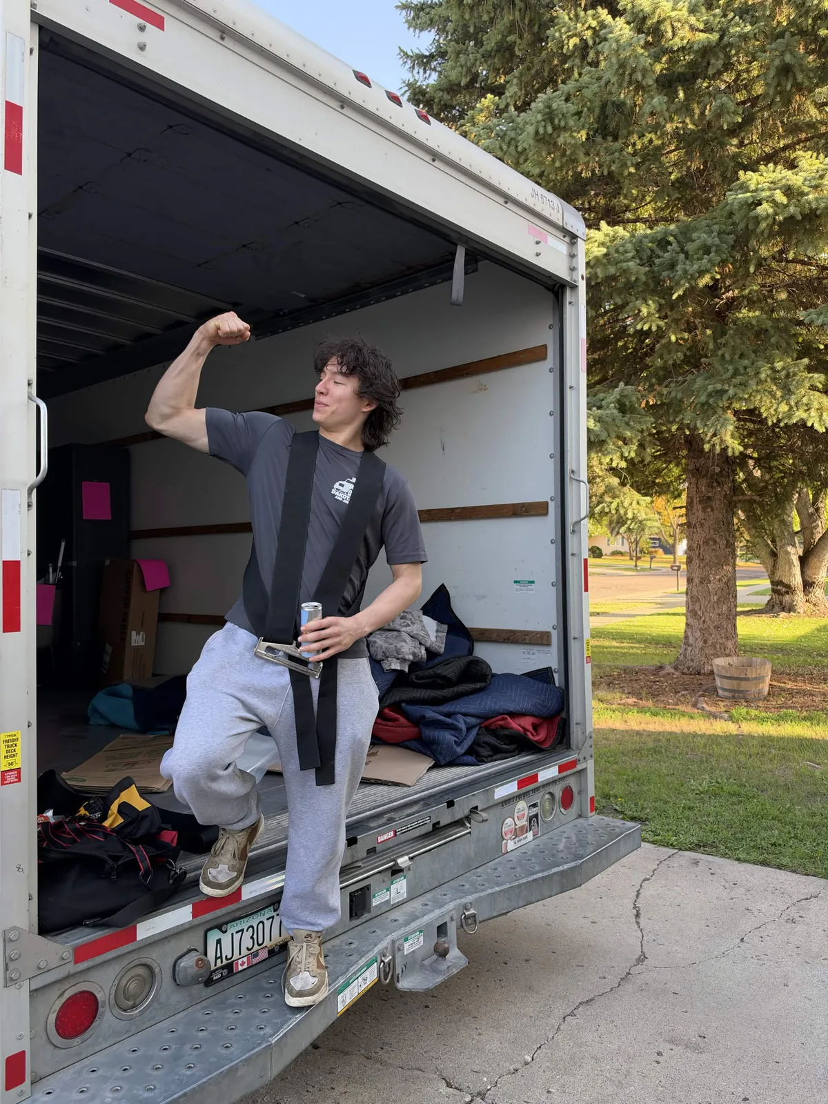Dakota Moving and Junk Removal crew member flexing on the back step of an open moving truck while wearing a shoulder dolly, Fargo-Moorhead area.